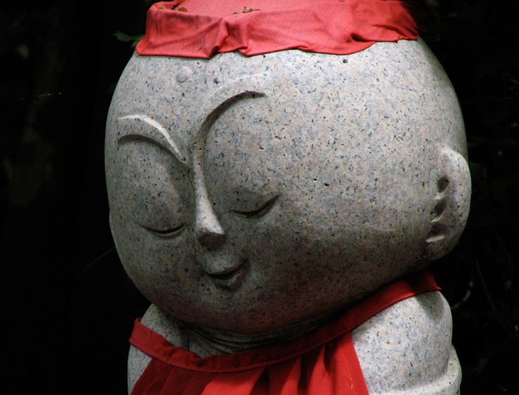 A carved stone jizo statue in Japan looking very happy with itself