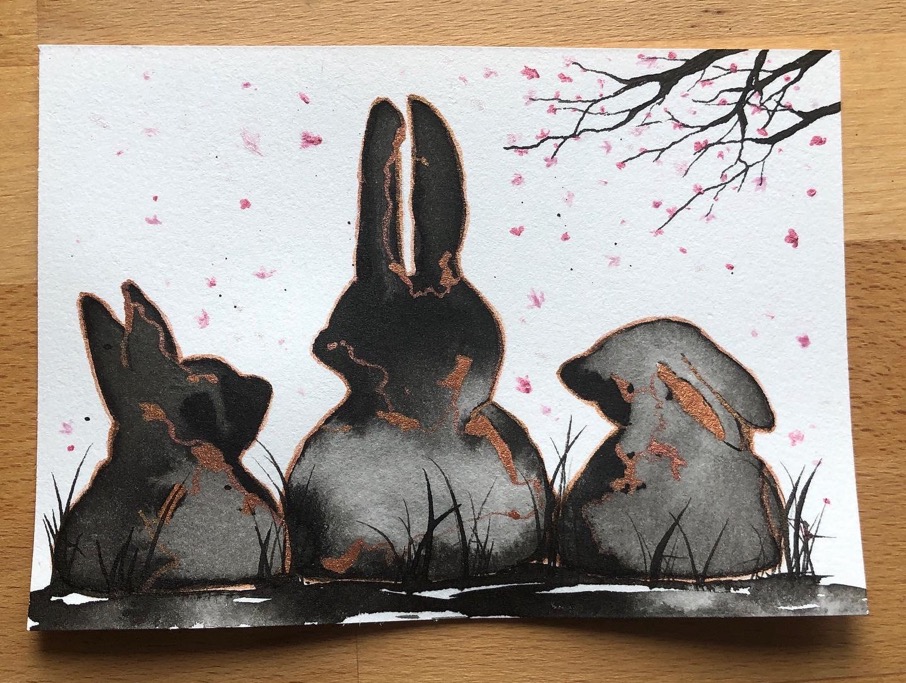 Three black ink-wash rabbits with rose-gold cracks under falling sakura blossoms, painted on textured cotton paper