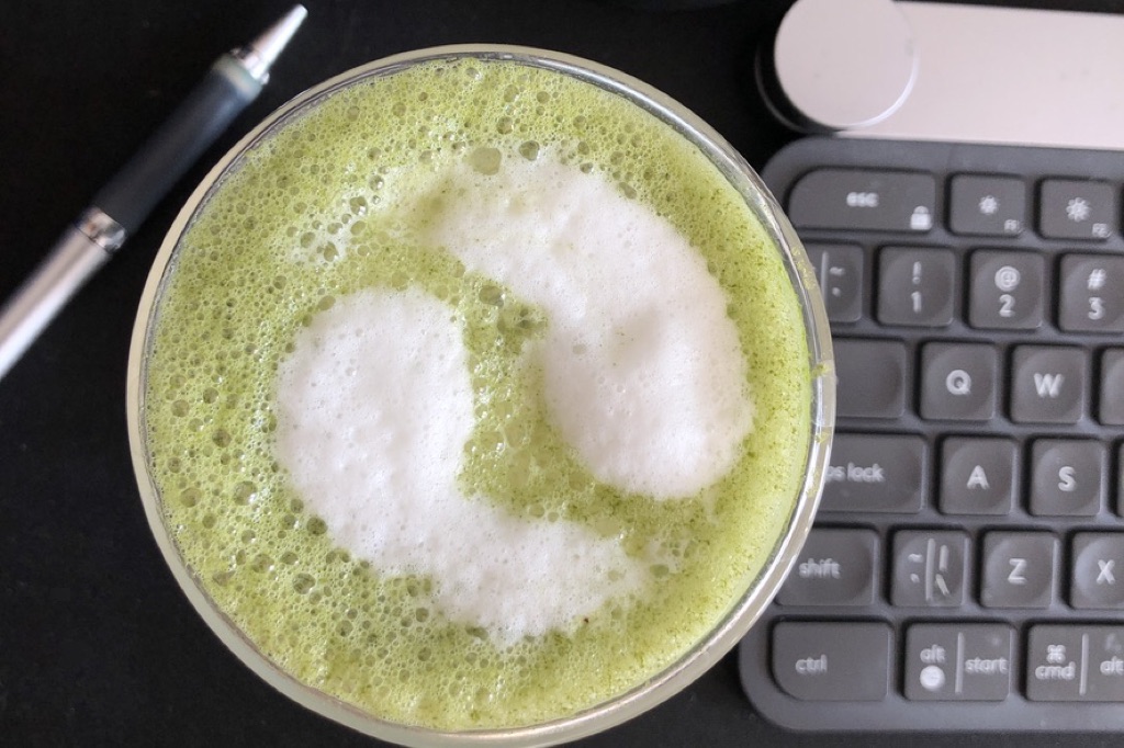A frothy matcha late with a yin-yang in white in the foam in a glass double-walled mug