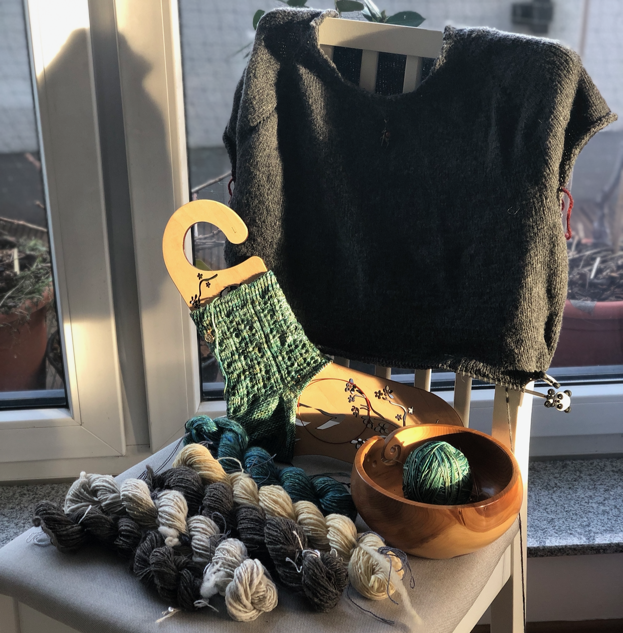 A number of yarn projects - knitting and spinning - are displayed on a kitchen chair in front of a balcony door.