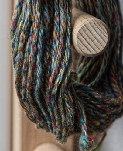 Handspun chain plied multicoloured wool hanging from a warping frame
